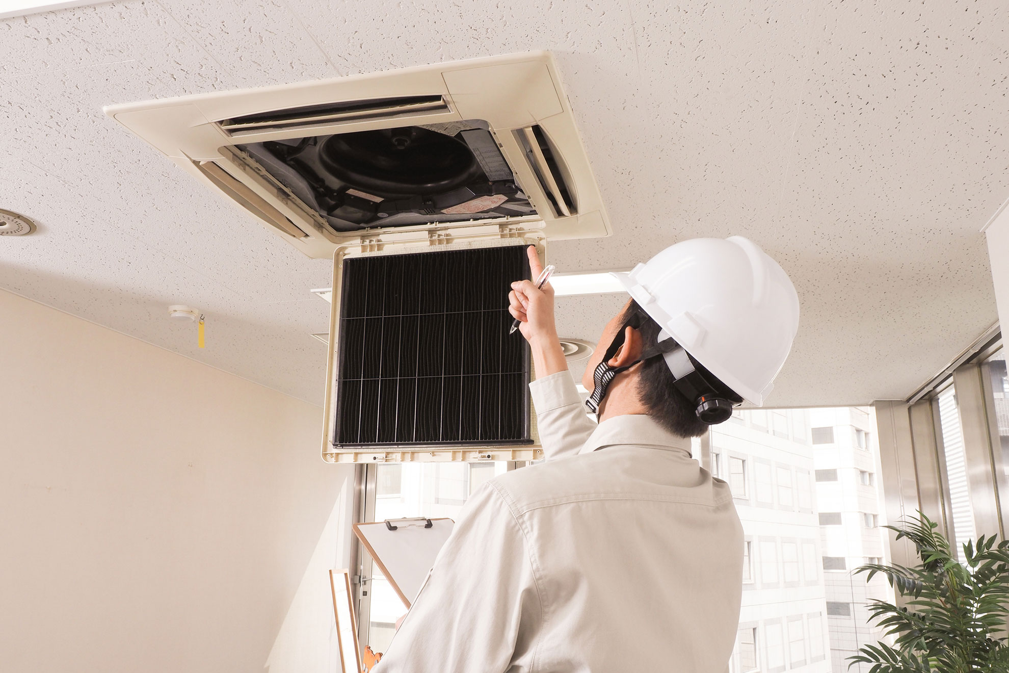 オフィスの業務用エアコンのチェックをしているヘルメットを被った作業員